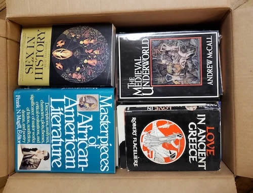 A cardboard box containing several books, including titles on sexual history, medieval underworld, and ancient Greek love.
