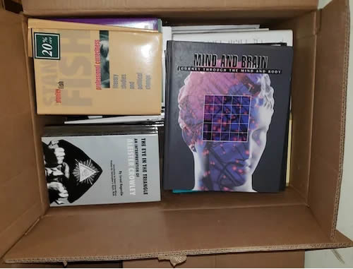 A cardboard box filled with various books, including titles on psychology and neuroscience, with a prominent cover featuring a head graphic.